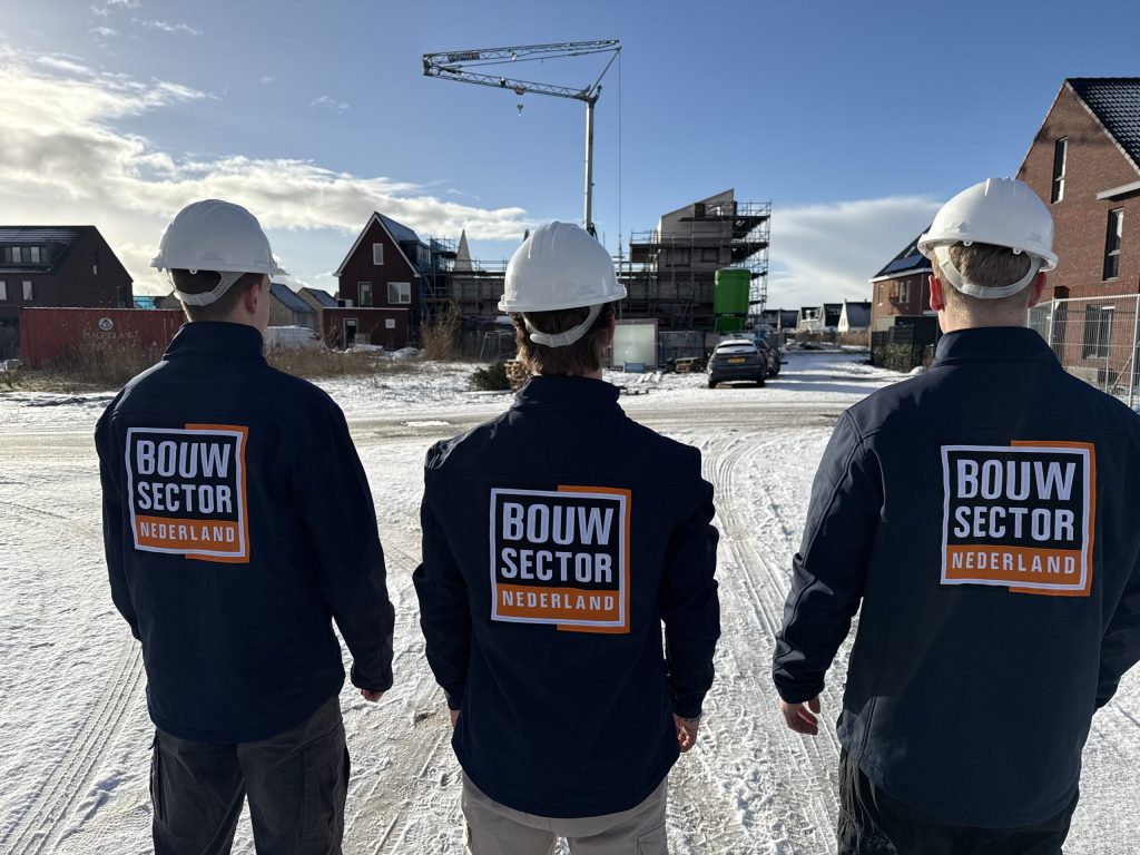 Drie vakmensen van Bouwsector Nederland met witte helm op weg naar een bouwplaats in de sneeuw